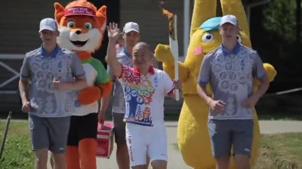 Minsk, Bielorussia - 19 luglio 2019: Un atleta asiatico con una fiamma olimpica in mano corre accompagnato da altri atleti e saluta con la mano — Video Stock