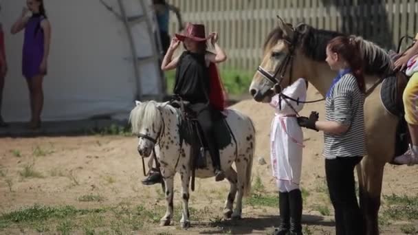 Mińsk, Białoruś - 19 lipca 2019: Mała piękna dziewczynka w długiej sukience na ranczu siedzi na kucyku i zdejmuje kapelusz — Wideo stockowe