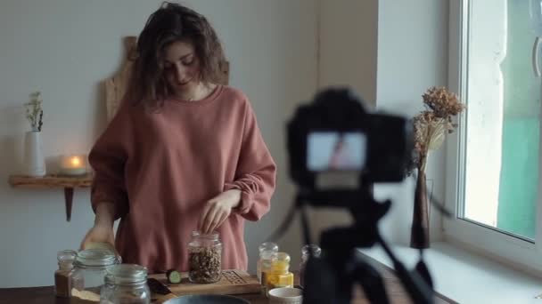美しい笑顔の女の子ブロガーの話と彼女のブログのためのカメラの前で料理のプロセスを示しています食品について — ストック動画
