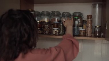 Genç ve güzel bir kız mutfak dolabından bir kavanoz fındık alır ve onları gülerek yer.