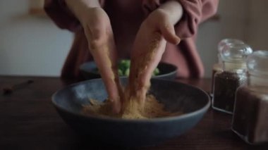 Mutfaktaki genç bir kız büyük bir kasede brokoli için elleriyle karıştırıyor. Yakın plan.