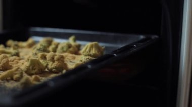 Kız daha fazla pişirmek için fırına brokoli ve baharat dolu bir tepsi koyar. Yakın plan.