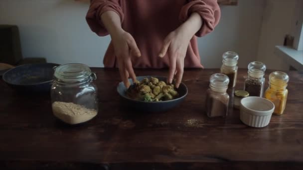 スパイスの瓶とキッチンテーブルでは、女の子の手はボウルにスパイスでブロッコリーを攪拌します。閉鎖 — ストック動画