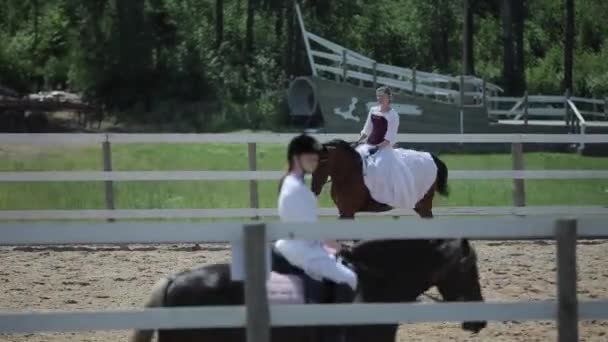 ミンスク,ベラルーシ- 19 7月2019:ヴィンテージ中世の長い白いドレスの美しい女の子は、他の女の子のライダーの間で柱に馬に乗る — ストック動画