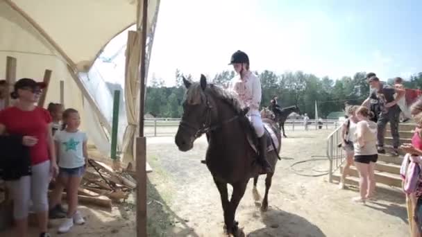 Minsk, Biélorussie - 19 juillet 2019 : Des spectateurs saluent une femme jockey en selle sur un cheval à l'entrée de l'arène intérieure d'un ranch équestre — Video