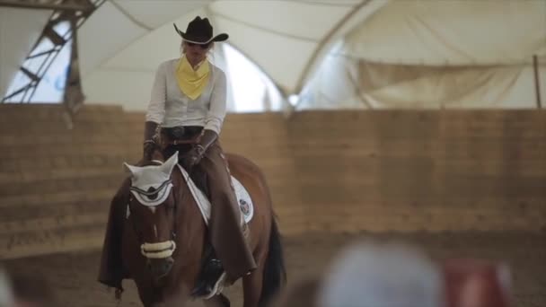 ミンスク、ベラルーシ- 19 7月2019:美しい馬の鞍のカウボーイスーツと眼鏡の素敵な若いブロンド。スローモーション。正面図 — ストック動画