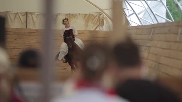 Minsk, Bielorussia - 19 luglio 2019: Una bella ragazza cavalca un cavallo in un lungo abito medievale vintage con corsetto e peli svolazzanti attraverso l'arena del ranch. Primo piano sfocato — Video Stock