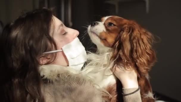 在家里检疫的时候，戴着防护面罩，抱着她的狗，笑着美丽的小女孩。检疫活动。Coronavirus.COVID-19 — 图库视频影像