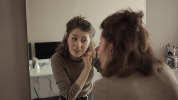 Egy fiatal lány a tükör előtt megvizsgálja a haját és kihúzza az ősz haját. — Stock videók