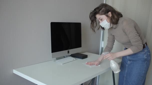 Una giovane ragazza attraente in una maschera protettiva quarantena pulisce accuratamente il computer con un disinfettante.Coronavirus. COVID-19 — Video Stock