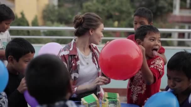 Katmandu, Nepal - 23 november 2019: En kaukasisk kvinna som leker med nepalesiska barn. Spränga ballonger tillsammans. Glada asiatiska barn. — Stockvideo