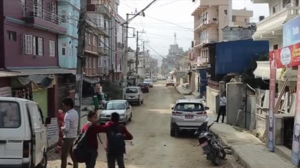 Kathmandu, Nepal - 23 de novembro de 2019: Uma típica rua asiática nepalesa. Poucas pessoas a andar. Pobre arquitetura. Duas pupilas, meninos de uniforme andando . — Vídeo de Stock