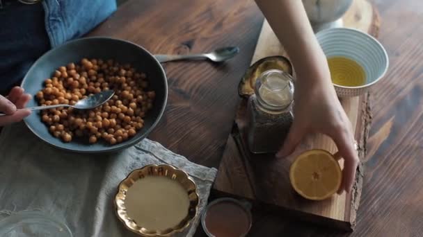 女の子の近くに手作りのフムスを作るためのひよこ豆とボウルにレモンからジュースを絞る手 — ストック動画