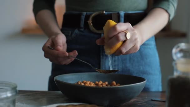 Een jong meisje perst sap uit een citroen en voegt het toe aan de kom met kikkererwten om thuis hummus te bereiden. Close-up — Stockvideo