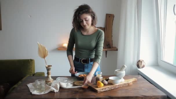 Giovane bella ragazza a un tavolo nella sua cucina mescola gli ingredienti per cucinare hummus tradizionale — Video Stock