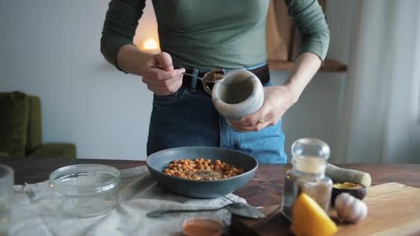 Kız nohutlu bir kaseye yer baharatı koyuyor. Evde geleneksel humus pişirmek. Yakın plan. — Stok video