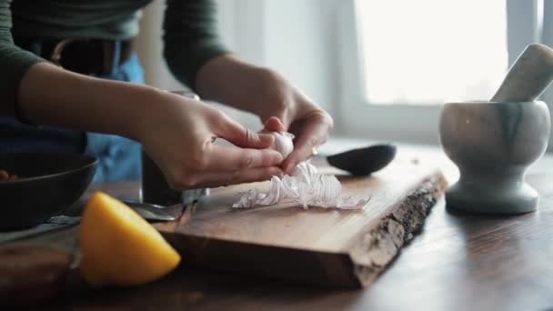 Bir kız geleneksel humus pişirmek için malzemelerin karışımına eklemek için mutfak masasına sarımsak soyuyor. Yakın plan. — Stok video