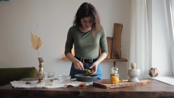 Schöne junge Mädchen lächelt, während sie an einem Tisch in ihrer Küche steht und hausgemachten Hummus zubereitet — Stockvideo