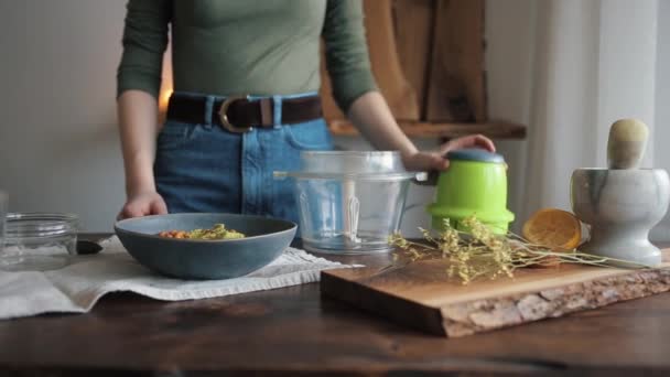 Giovane ragazza al tavolo della cucina diffonde gli ingredienti in un frullatore da una ciotola per cucinare hummus tradizionale. Primo piano — Video Stock