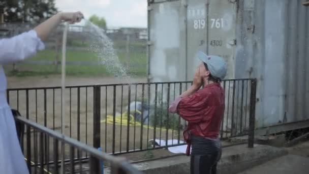 Minsk, Weißrussland - 19. Juli 2019: Ein Mädchen im Teenageralter lacht und wirbelt an einem heißen Sommertag an der frischen Luft unter der Wasserspritze aus einem Schlauch. Nahaufnahme — Stockvideo