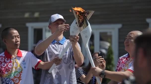 Minsk, Bielorrusia - 19 de julio de 2019: Un atleta asiático con una antorcha de llama olímpica en sus manos corre acompañado por otros atletas y agita su mano en un saludo — Vídeos de Stock