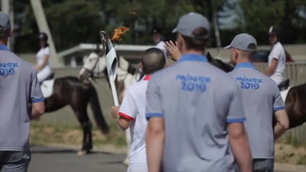 Minsk, Biélorussie - 19 juillet 2019 : Un athlète asiatique avec une flamme olympique dans les mains court accompagné d'autres athlètes et salue sa main — Video
