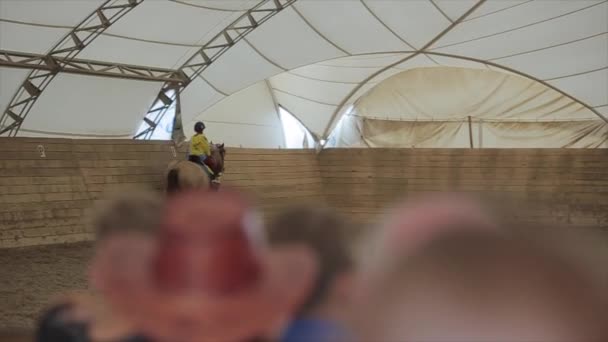 Minsk, Biélorussie - 19 juillet 2019 : Une petite fille chevauchant un cheval lors d'une compétition d'équitation monte et s'incline devant le public. Premier plan flou — Video