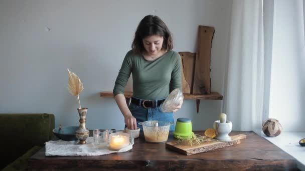 예쁜 한 소녀 는개가 식탁에 앉아서 자기를 지켜보는 동안 믹서에 향료를 첨가하여 부식토를 준비 한다 — 비디오