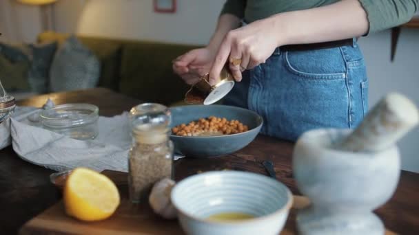 A young girl mixes the ingredients in a bowl to cook traditional chickpea hummus at home. Close-up — Stock Video