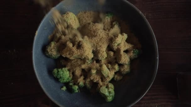Close-up of broccoli in a bowl on the kitchen table and strewd with a mixture of seasoning for cooking — Stock Video