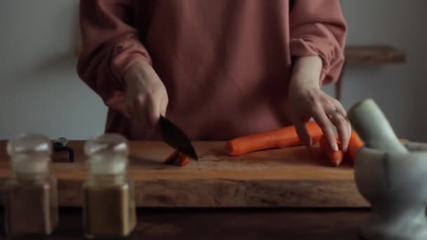 Großaufnahme der Hände einer jungen Frau, die mit einem großen Messer Karotten hackt, um in ihrer Küche zu kochen — Stockvideo