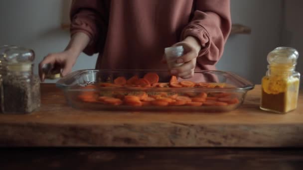 A menina na mesa da cozinha debulha especiarias em um morteiro ao lado de uma tigela de vidro de cenouras picadas. Close-up — Vídeo de Stock