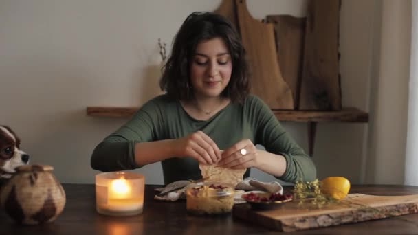 Uma menina bonita nova come o hummus cozinhado por ela e seu cão senta-se na mesa da cozinha e observa-a. Close-up — Vídeo de Stock