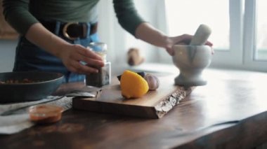 Bir kız geleneksel humus pişirmek için malzemelerin karışımına eklemek için mutfak masasına sarımsak soyuyor. Yakın plan.