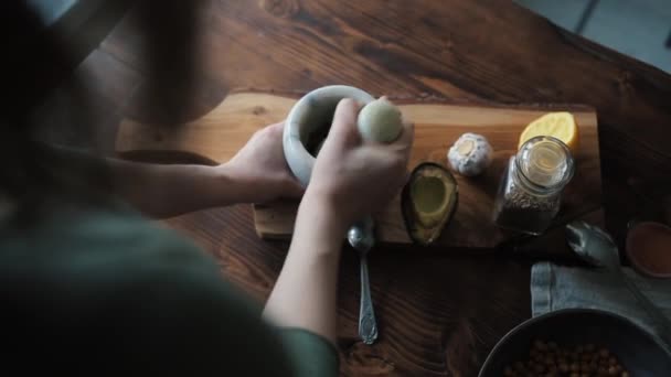 Seorang gadis muda menggiling rempah-rempah dalam mortir untuk menambahkan mereka ke mangkuk dengan kacang arab dan membuat hummus buatan sendiri. Lihat dari atas. Close-up — Stok Video