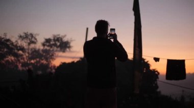 Gün batımının, güneşin doğuşunun fotoğraflarını çeken bir adamın silüeti. Köy, çamaşırhane açık havada kuruyor..