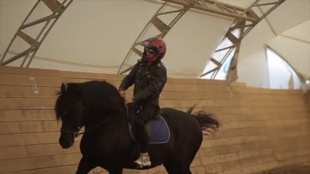 Minsk, Vitryssland - 19 juli 2019: Killen i motorcykelhjälmen rider en vacker mörk häst på en täckt arena stannar sedan och bugar — Stockvideo