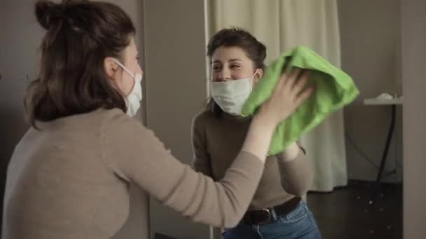 Een jong Europees meisje met een beschermend masker veegt een spiegel af met een ontsmettingsmiddel dat thuis in quarantaine zit.Coronavirus. COVID-19 — Stockvideo