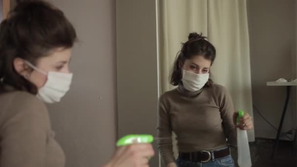 Een jong Europees meisje met een beschermend masker veegt een spiegel af met een ontsmettingsmiddel dat thuis in quarantaine zit.Coronavirus. COVID-19 — Stockvideo