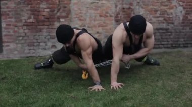 Erkekler egzersiz ve egzersiz yapar. Bir yandan eşzamanlı şınav çeken iki genç kaslı adam yerden. Kamera aşağı yukarı hareket ediyor..