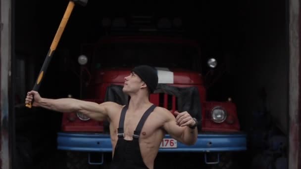 Jeune pompier musclé entraînement extrême avec un marteau la tient au-dessus de la tête sur le fond d'un camion de pompiers — Video