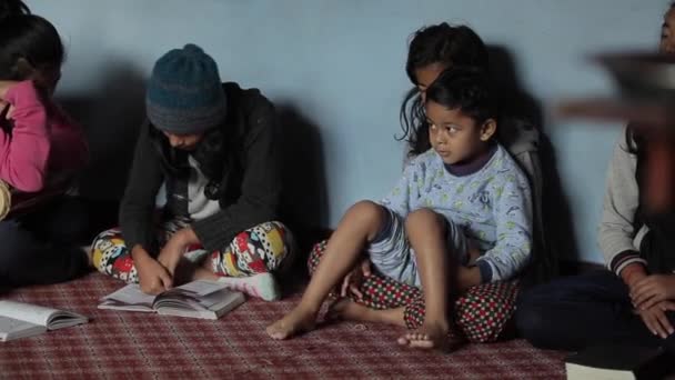 Катманду, Непал - 22 ноября 2019 года: Азиатский индийский непальский мальчик сидит в комнате рядом с девочками, которые сидят на полу комнаты, читая книги. Крупный план — стоковое видео