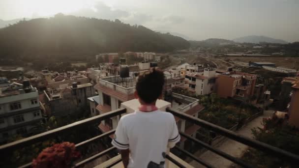 Zadní pohled na nepalského chlapce, jak se dívá na domy Káthmándú z balkónu. — Stock video