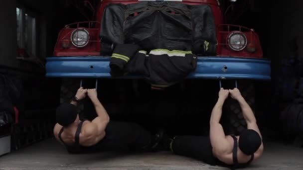 Szélsőséges gyakorlatokat és edzéseket végző férfiak.Két izmos fiatal tűzoltót egyszerre húznak a karjukba, egy tűzoltóautó lökhárítójába kapaszkodva. — Stock videók
