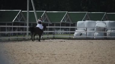 Minsk, Belarus - 19 Temmuz 2019: Birbirinin aynısı elbise ve çelenk giymiş genç kızlar at çiftliğinin açık arenasında at sırtında birbirlerine doğru ilerliyorlar.