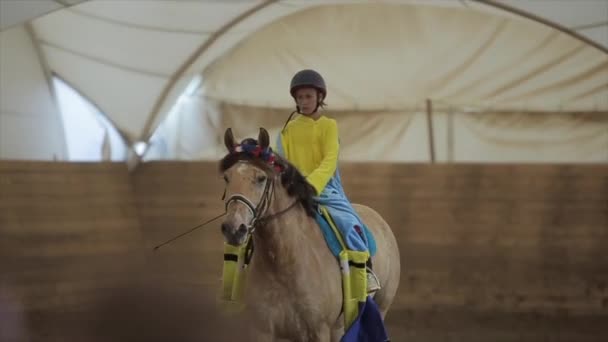 Mińsk, Białoruś - 19 lipca 2019: Mała urocza dziewczynka ujeżdżająca konia w stroju sługusa na krytym zagrodzie rancza konia — Wideo stockowe