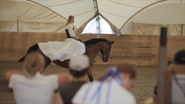 Minsk, Bielorrússia - 19 de julho de 2019: Jovem em vestidos e grinaldas idênticos em suas cabeças montam um em direção ao outro em cavalos na arena aberta de um rancho de cavalos — Vídeo de Stock