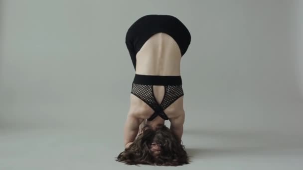 Egy fiatal lány fejenállás közben jógázik. A kamera alulról felfelé mozog. — Stock videók