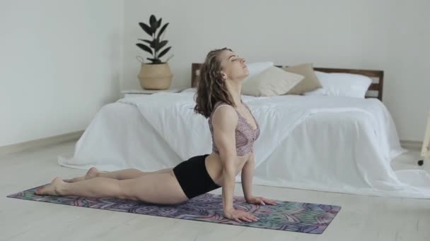 Jovem bela garota pratica poses de ioga deitado em um tapete em seu quarto em um sutiã esportivo e cuecas. Mulher fazendo ioga em casa durante a quarentena . — Vídeo de Stock