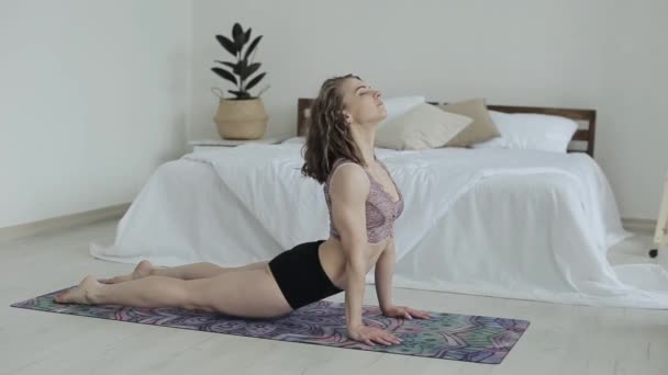 Tânăra fată frumoasă practică yoga pozează întinsă pe un covor în camera ei într-un sutien sportiv și chiloți. Femeia care face yoga acasă în timpul carantinei . — Videoclip de stoc